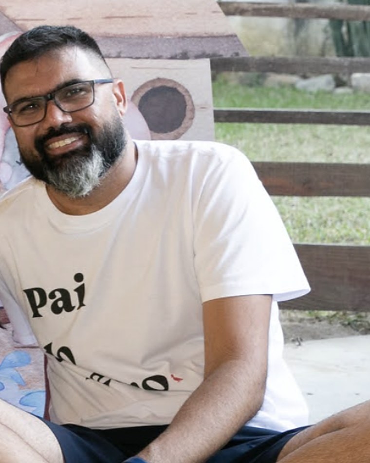 Rafael França sorrindo, sentado no chão, de camiseta branca